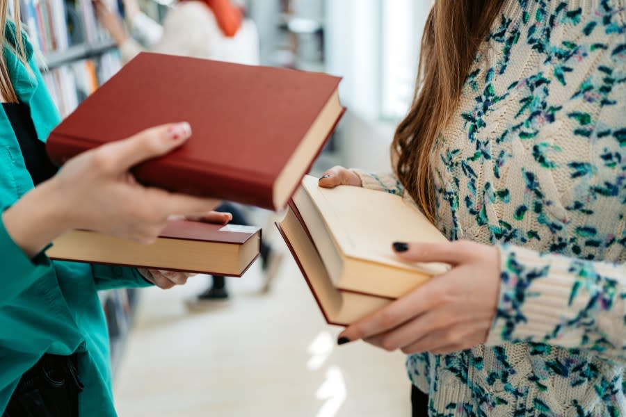 Two students exchanging books in a library.