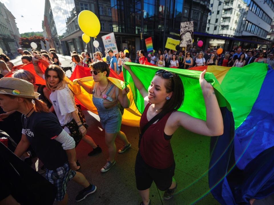 People hold a giant pride flag over their heads during a parade.