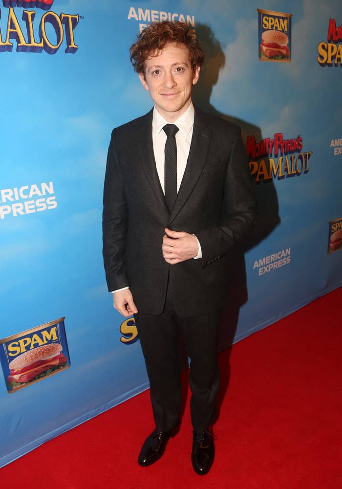 Ethan in a dark suit with tie smiling at a Monty Python's Spamalot event