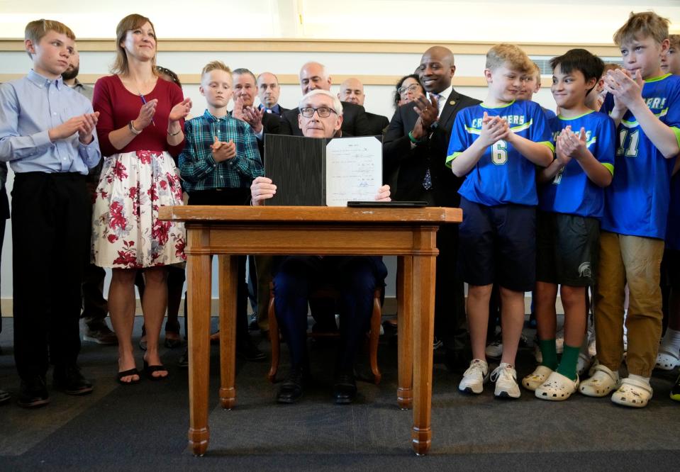 Wisconsin Gov. Tony Evers holds up one of the two signed reckless driving bills he signed into law as he’s surrounded by family and friends of Milwaukee area pastor, Rev. Aaron Strong, including Strong’s wife, Abbie Strong (upper, second left), who was killed by a reckless driver. Evers signed the bills at The Grace Center in Milwaukee on Wednesday, May 10, 2023.