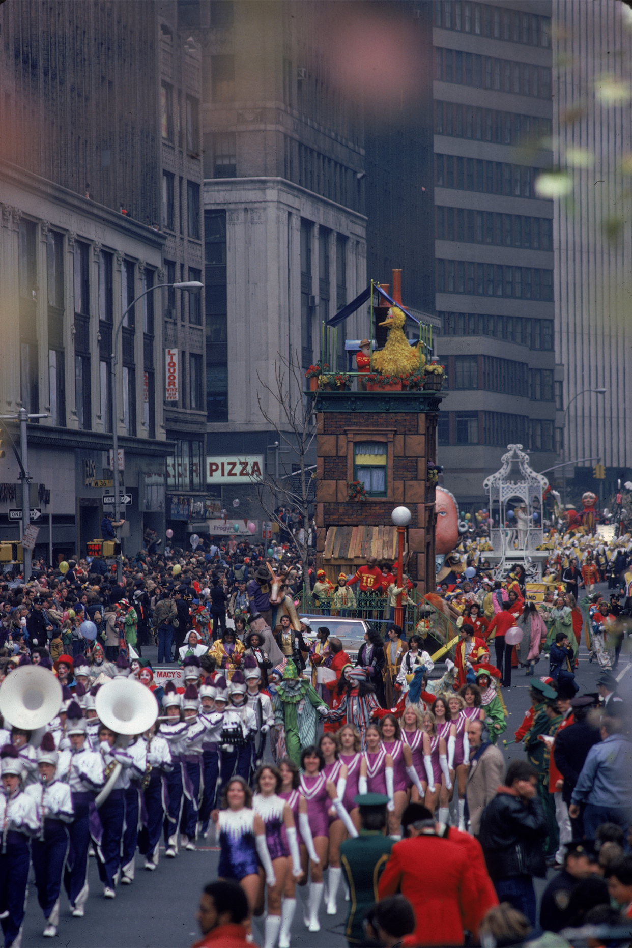 A marching band moves down the street followed by a Sesame Street float as crowds look on from the sidelines during the Macy's Thanksgiving Day Parade