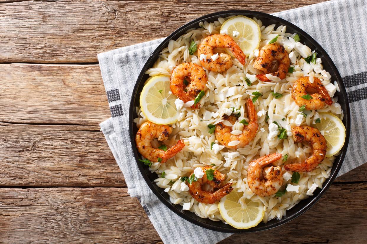 Mediterranean food Pasta orzo with grilled shrimps, feta cheese and lemon close-up on a plate on the table. horizontal top view from above