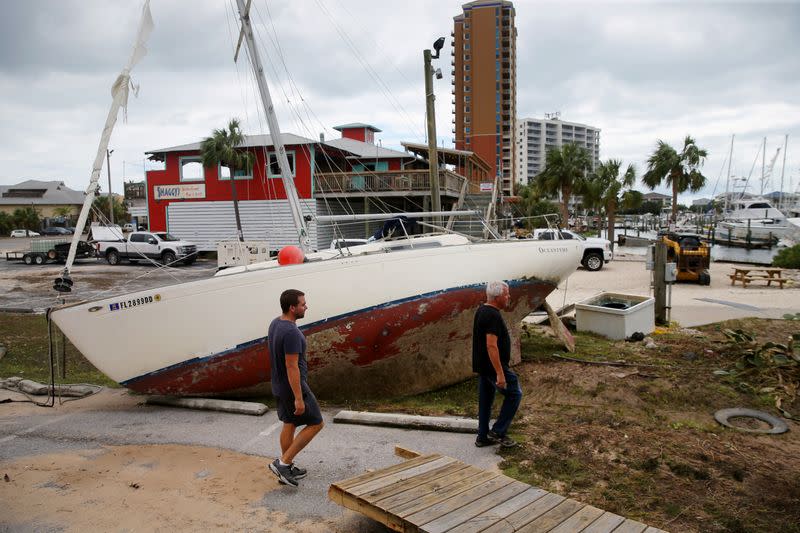 People walk past a boat washed ashore after Hurricane Sally in Pensacola Beach