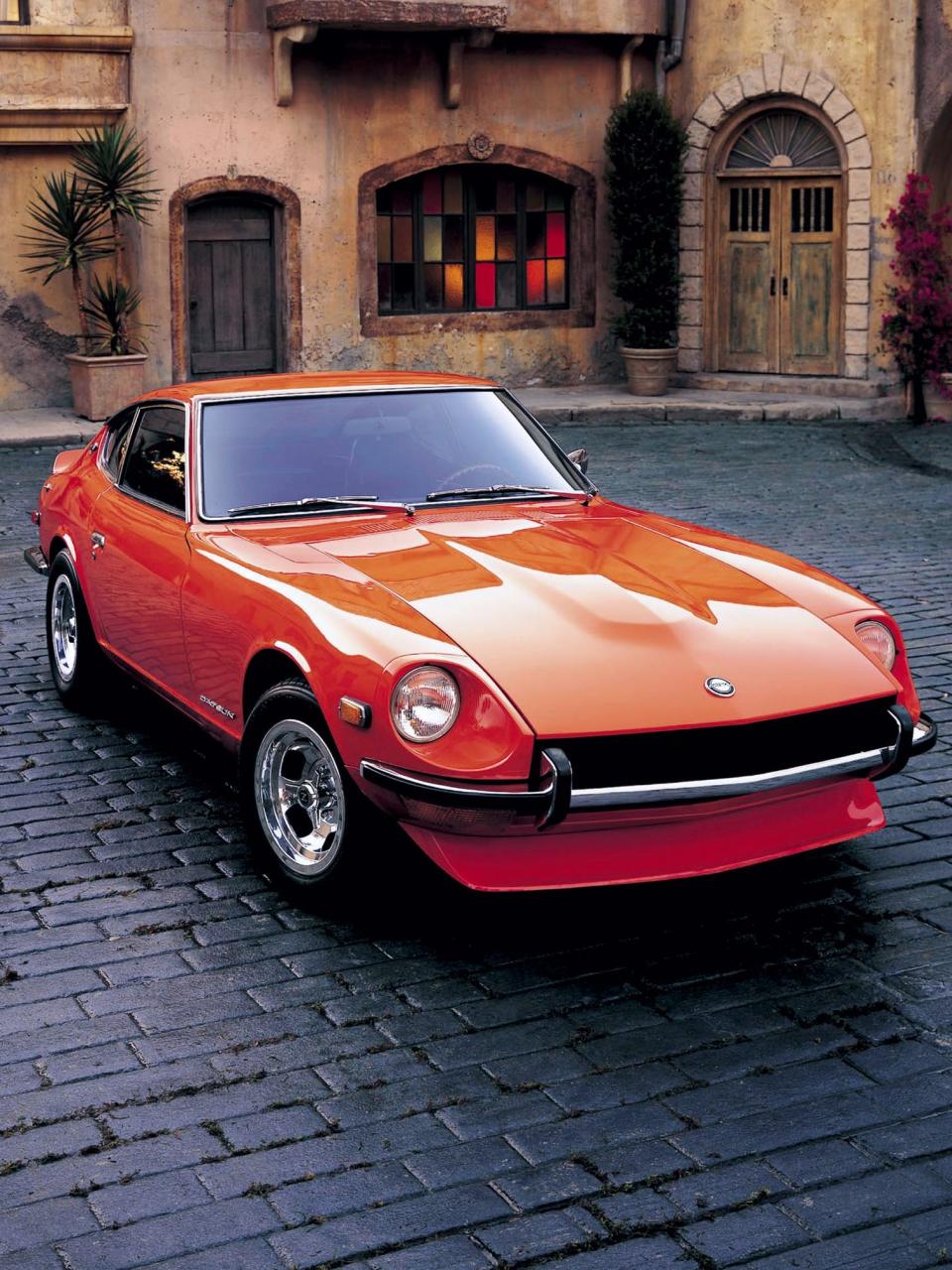 An orange 1970 Datsun 240Z sports car parked in front of a building.