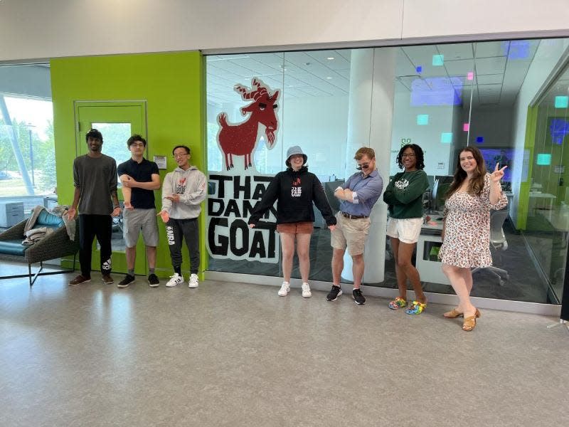 RIT students stand in front of a sign for 'That Damn Goat', a game produced by students and faculty in MAGIC Spell Studios.