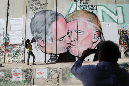 A man photographs a woman as she stands next to a mural depicting U.S. President Donald Trump and Israeli Prime Minister Benjamin Netanyahu on the controversial Israeli barrier, in the West Bank city of Bethlehem October 29, 2017. REUTERS/Ammar Awad
