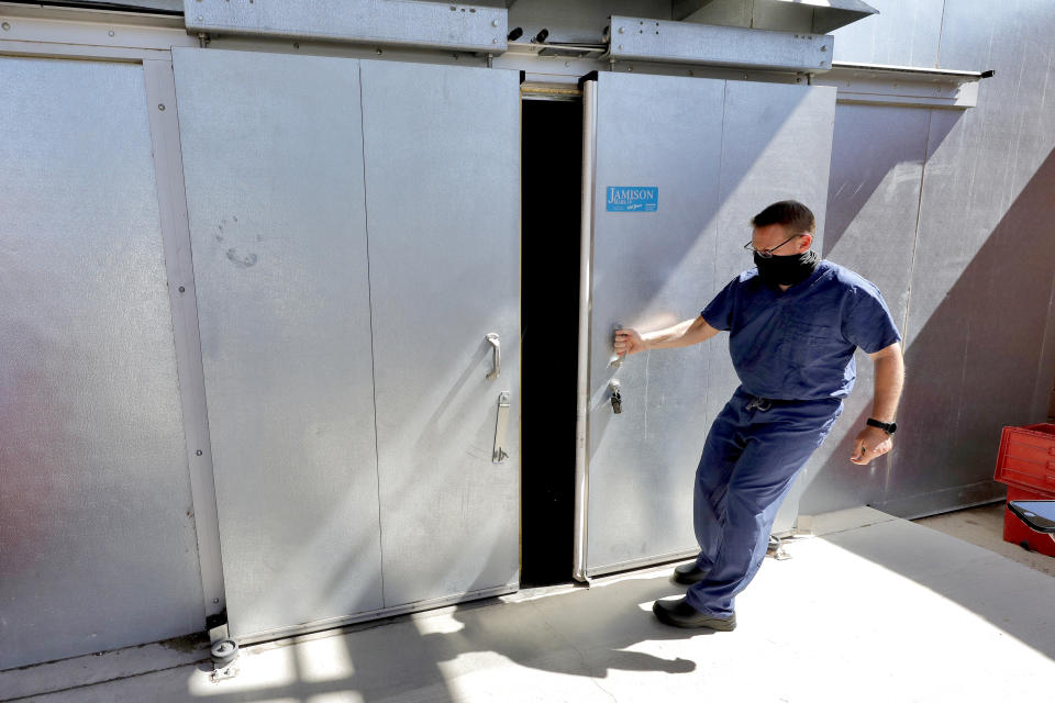 FILE - In this July 29, 2020, file photo, Pima County Medical Examiner Dr. Greg Hess opens the overflow body storage cooler at the medical examiner's office in Tucson, Ariz. After a record hot and dry summer, more deaths among border-crossers have been documented in Arizona's desert and mountains. The office of Dr. Hess works with the nonprofit Humane Borders in Tucson to map the recoveries of migrants who die along Arizona's entire border region. (AP Photo/Matt York, File)