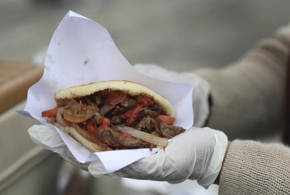 In this June 12, 2019 photo, Venezuelan Arepa's vendor Yuleiny Mendoza displays one her street food creation at a street corner in Lima, Peru. The arepa's surge on the world stage comes as consumption of the bread steadily declines back home amid a punishing financial crisis worse than the U.S. Great Depression, leading an estimated 4 million people to flee. (AP Photo/Martin Mejia)