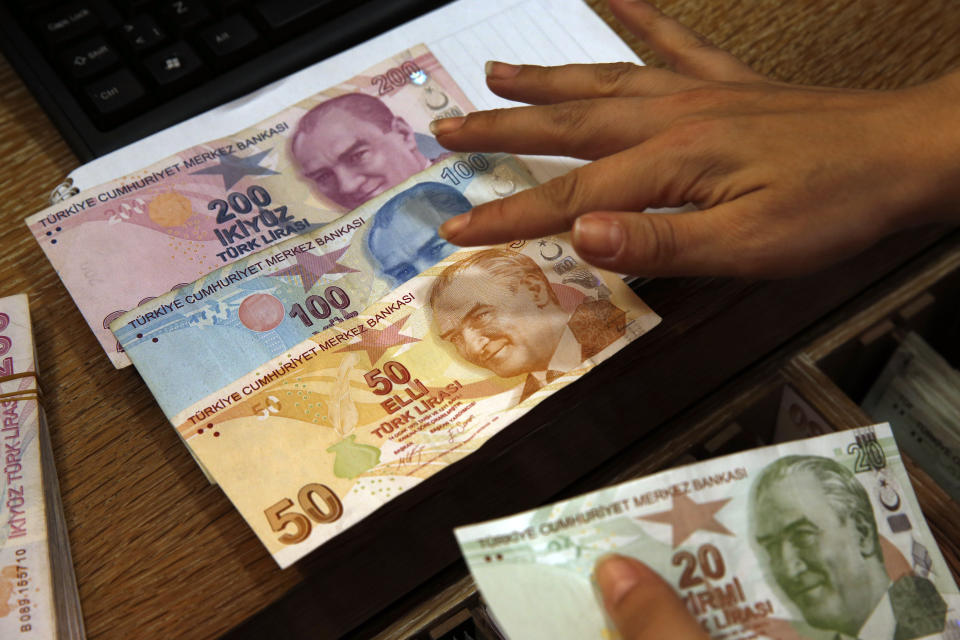 FILE- In this Wednesday, Aug. 15, 2018, file photo a worker at a currency exchange shop exhibits Turkish lira banknotes bearing pictures of modern Turkey's founder Mustafa Kemal Ataturk, in Istanbul. Investors have been pulling out of Turkey’s markets, sending its stock market and currency plunging. That’s making debt that Turkish companies owe in dollar terms even more expensive to pay back, which only further weakens the country’s financial system. (AP Photo/Lefteris Pitarakis, File)