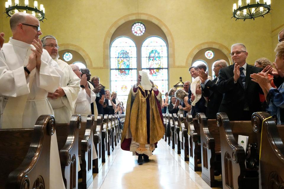 The Rev. Earl K. Fernandes, center, walks by pews holding a message from Pope Francis during his ordination and installation as the 13th bishop of the Diocese of Columbus.