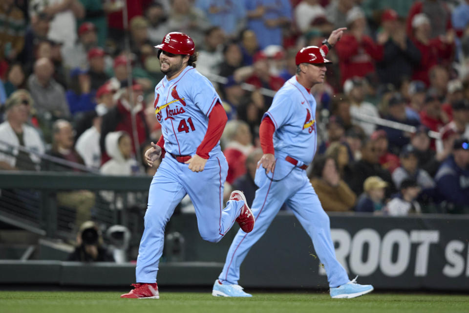 St. Louis Cardinals' Alec Burleson heads past third base coach Ron "Pop" Warner on the way home to score on a double by Willson Contreras against the Seattle Mariners during during the third inning of a baseball game Saturday, April 22, 2023, in Seattle. (AP Photo/John Froschauer)