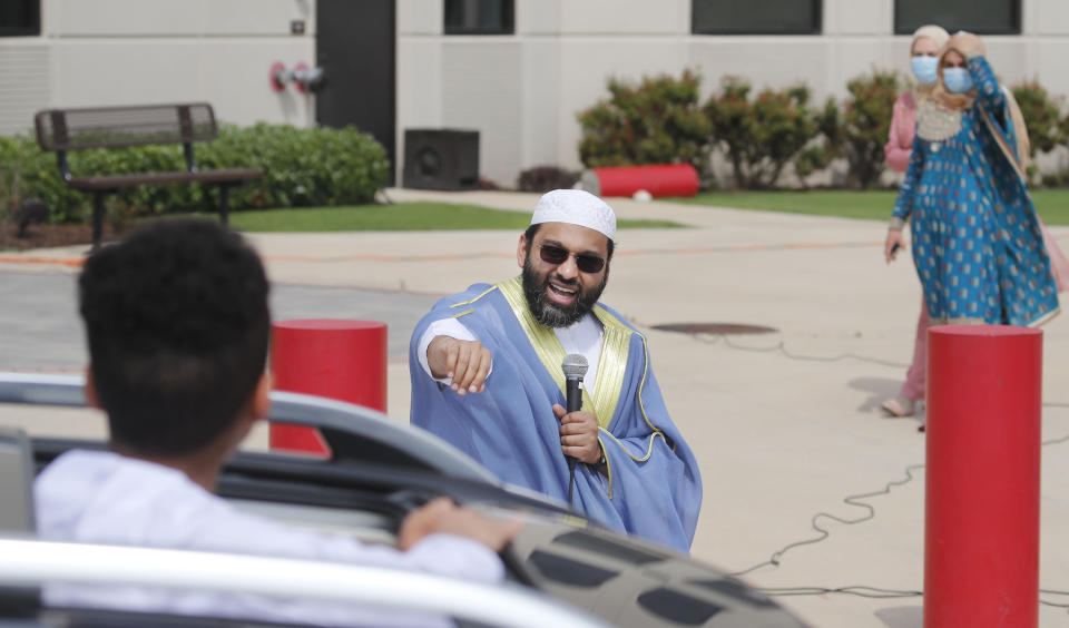 Sheikh Yasir Qadhi, center, speaks to a passing child during an Eid al-Fitr drive through celebration outside a closed mosque in Plano, Texas, Sunday, May 24, 2020. Many Muslims in America are navigating balancing religious and social rituals with concerns over the virus as they look for ways to capture the Eid spirit this weekend. (AP Photo/LM Otero)