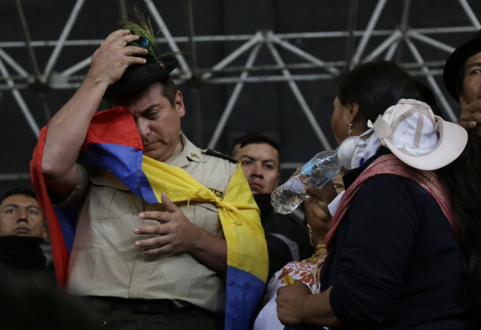 Col. Cristian Rueda Ramos, one of several police officers who has been detained by anti-governments protesters, is made to don a national flag as a cape and a fedora-styled hat, while standing on a stage at the Casa de Cultura in Quito, Ecuador, Thursday, Oct. 10, 2019. Thousands of protesters staged anti-government rallies Wednesday, seeking to intensify pressure on Ecuador's president after a week of unrest sparked by fuel price hikes. (AP Photo/Dolores Ochoa)