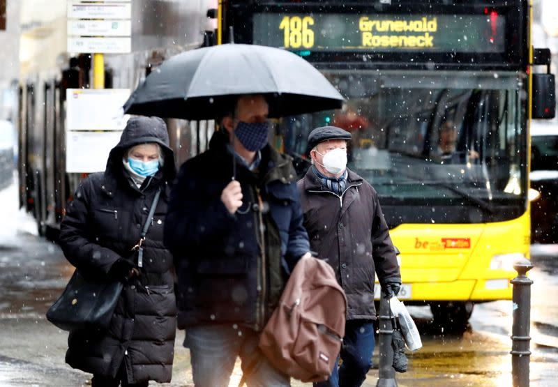 People wear face masks as they walk past a bus in Berlin