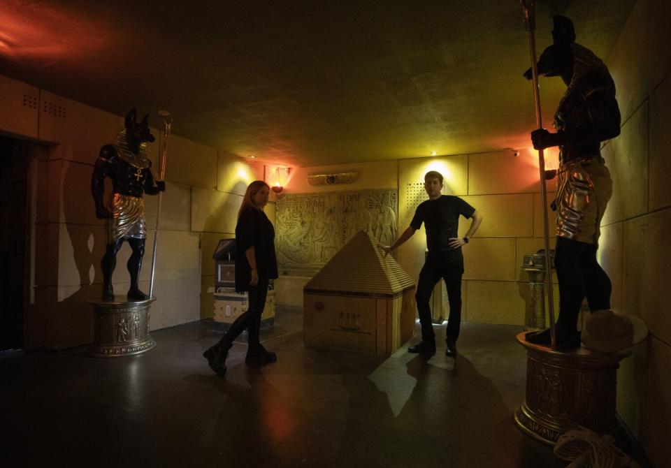 A woman and a man posing in a dark room with a pyramid and animal statues