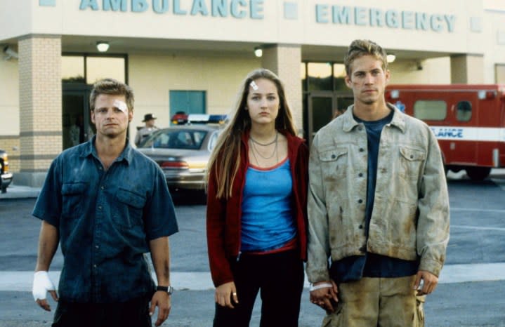 Three people with bandages on their body stand in a parking lot.