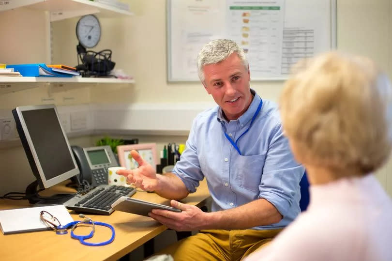 A male doctor sat at his desk in his office talking to a woman patient