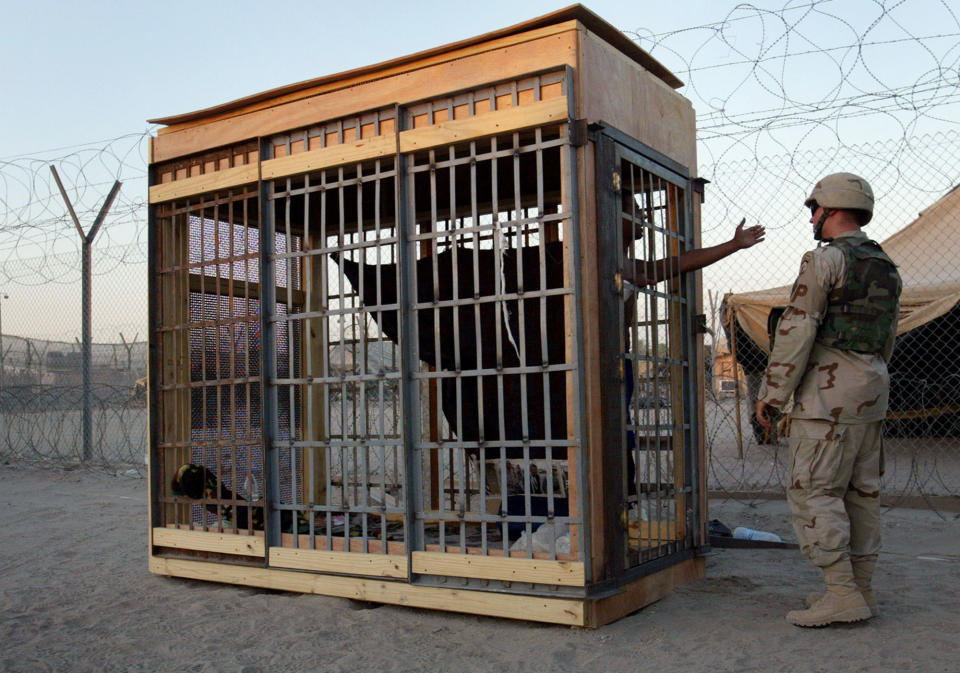 FILE - In this June 22, 2004 file photo, a detainee in an outdoor solitary confinement cell talks with a military policeman at the Abu Ghraib prison on the outskirts of Baghdad, Iraq. An Iraqi Justice Ministry official said Wednesday, April 16, 2014 that this week's closure of the infamous Abu Ghraib prison west of Baghdad is temporary and that it will be reopened once the security situation in the surrounding area is stable. The closure is the latest chapter in the history of the prison, which during Saddam Hussein's rule was one of the main facilities for jailing and executing his opponents. After the U.S.-led invasion that toppled Saddam, Abu Ghraib became notorious once again, for a 2004 scandal over abuses of detainees by American guards. (AP Photo/John Moore, File)