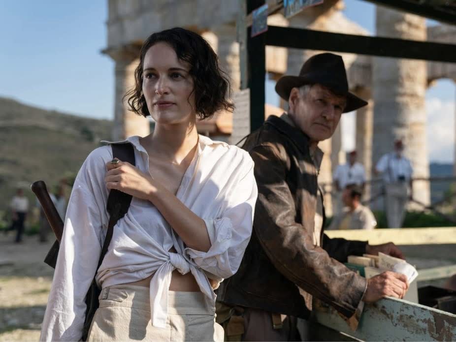 A screenshot from "Indiana Jones and the Dial of Destiny" where Harrison Ford is leaning against a fence while Phoebe Waller-Bridge is looking off into the distance.