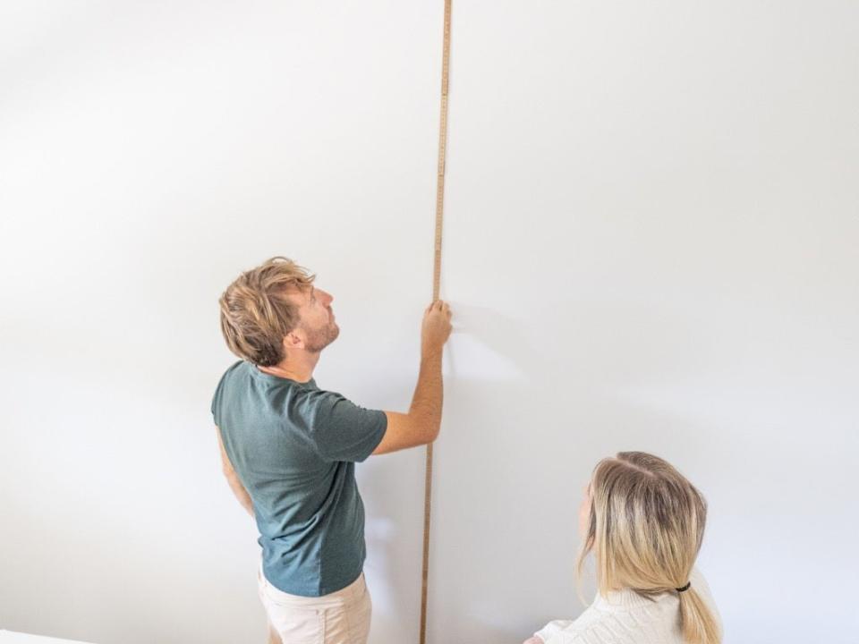 Man measuring ceiling height for Christmas tree as a woman looks on.