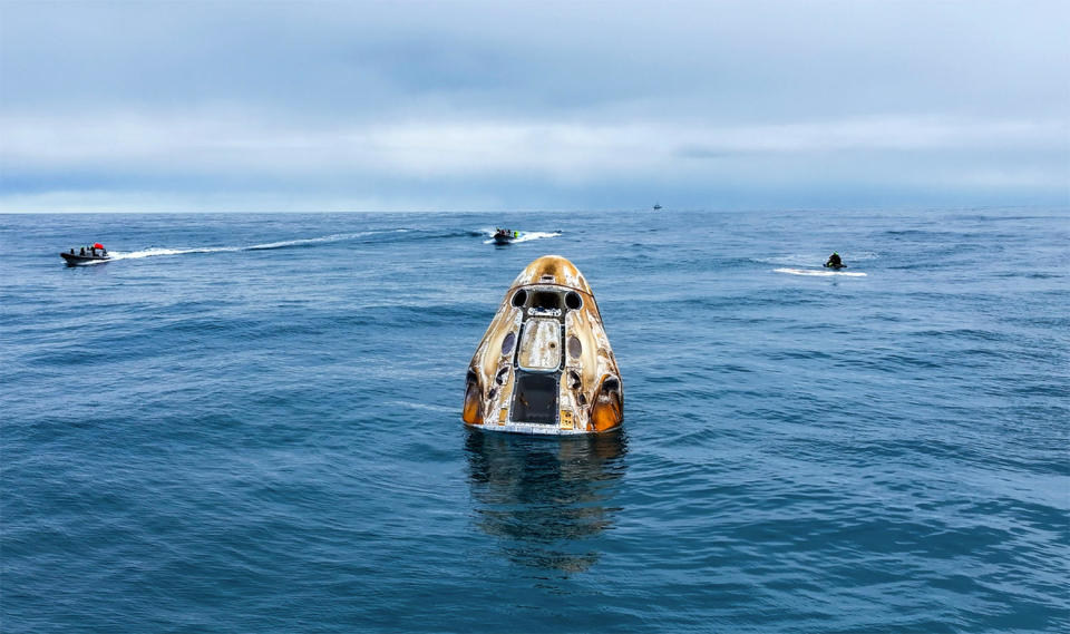 The Crew Dragon capsule, showing signs of re-entry heat, gently floats in the Atlantic Ocean as recovery crews assemble on the spacecraft.  / Credit: SpaceX