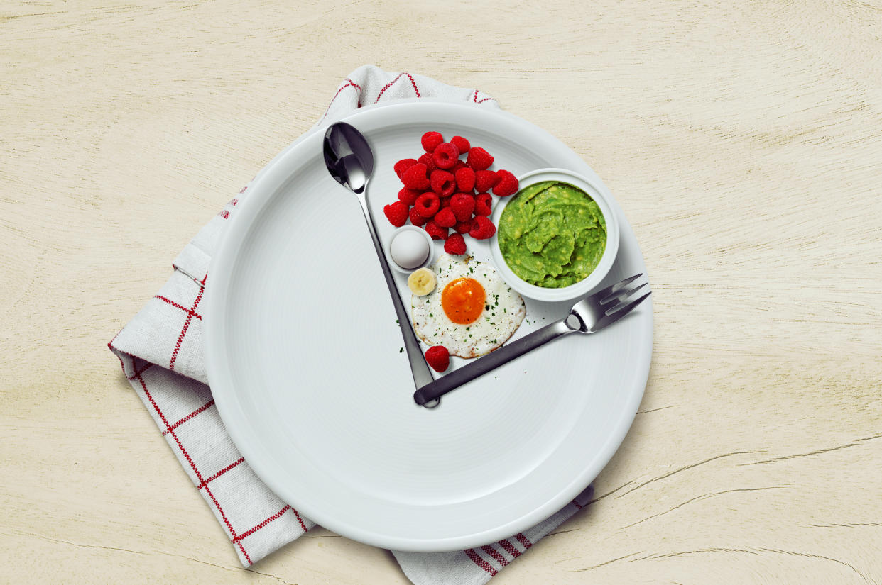 A white plate with cutlery sectioning off a part of the plate, with healthy foods in it like raspberries, a fried egg and smashed avocado