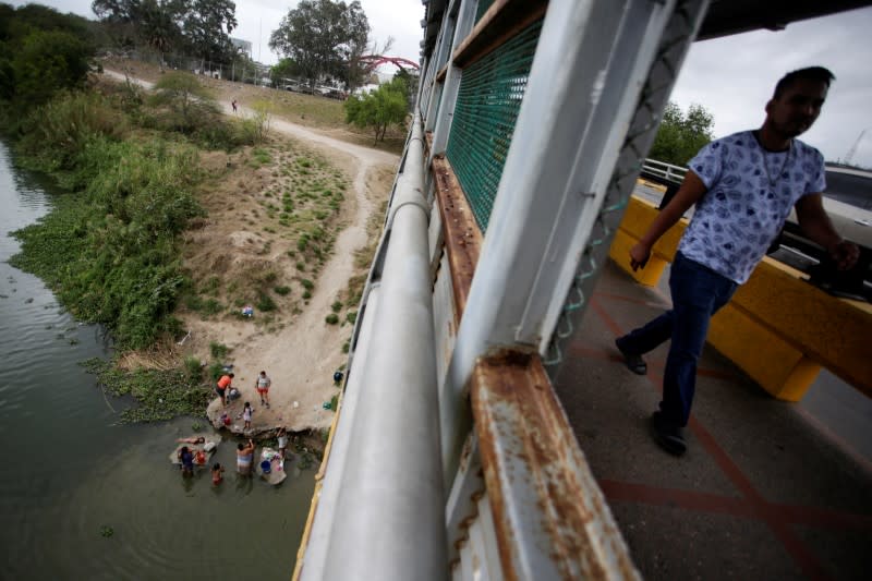 A man walks on the Matamoros-Brownsville International Bridge while migrants seeking asylum bath at the Rio Bravo river as local authorities prepare to respond to the coronavirus disease (COVID-19) outbreak, in Matamoros