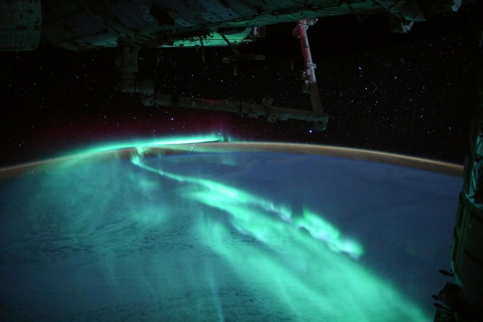 The international space station flying above bluish green auroras over Earth's southern hemisphere.