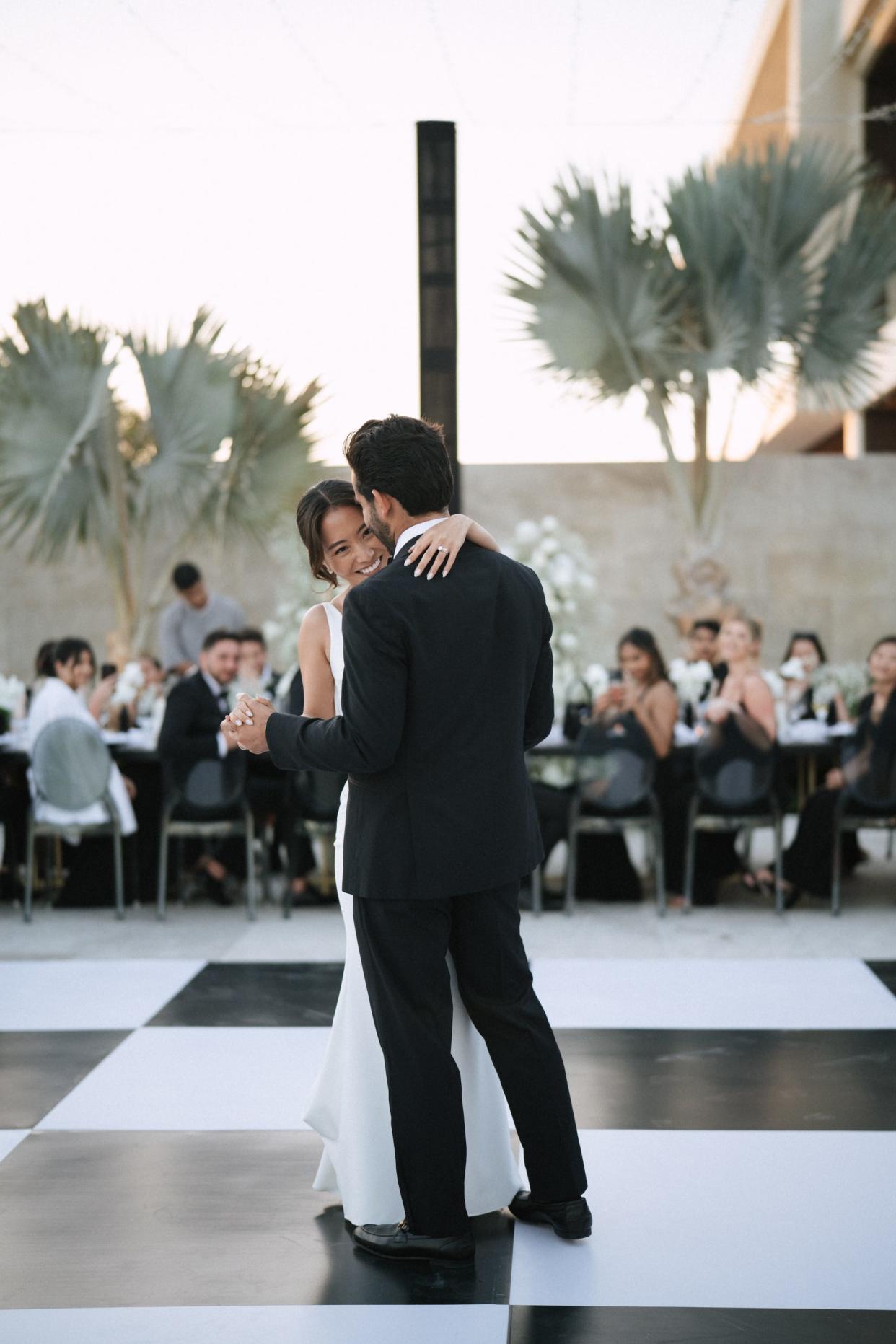 A bride laughs as she shares a first dance with her groom on a black and white dance floor.