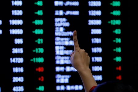 FILE PHOTO: A woman points to an electronic board showing stock prices as she poses in front of the board after the New Year opening ceremony at the Tokyo Stock Exchange (TSE), held to wish for the success of Japan's stock market, in Tokyo