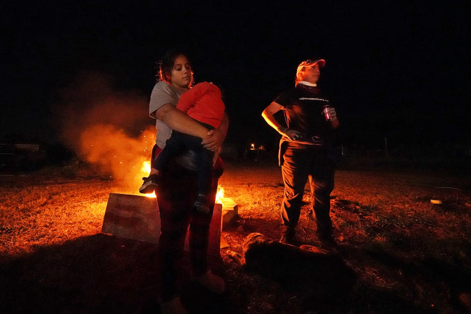 Katelyn Smith holds her one-year-old son son Ricky Trahan III, while talking with Tiffany Theriot, founder of the charity Cajun Commissary, as they stand next to a fire amidst the rubble of the family's destroyed home in Lake Charles, La., Friday, Dec. 4, 2020. They were hit by Hurricanes Laura and Delta. Her future in-laws are living in a tent on the property, while she, her child and her fiancé Ricky Trahan, Jr., are living in a camper loaned by Tiffany. A relatives home on the same property is now gutted and they are living in a camper as well. (AP Photo/Gerald Herbert)