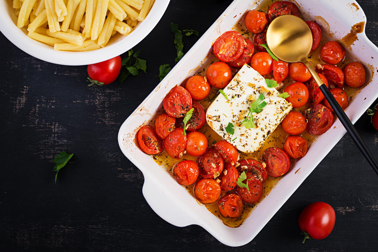 Fetapasta. Trending viral Feta bake pasta recipe made of cherry tomatoes, feta cheese, garlic and herbs in a casserole dish. Top view, above, copy space.