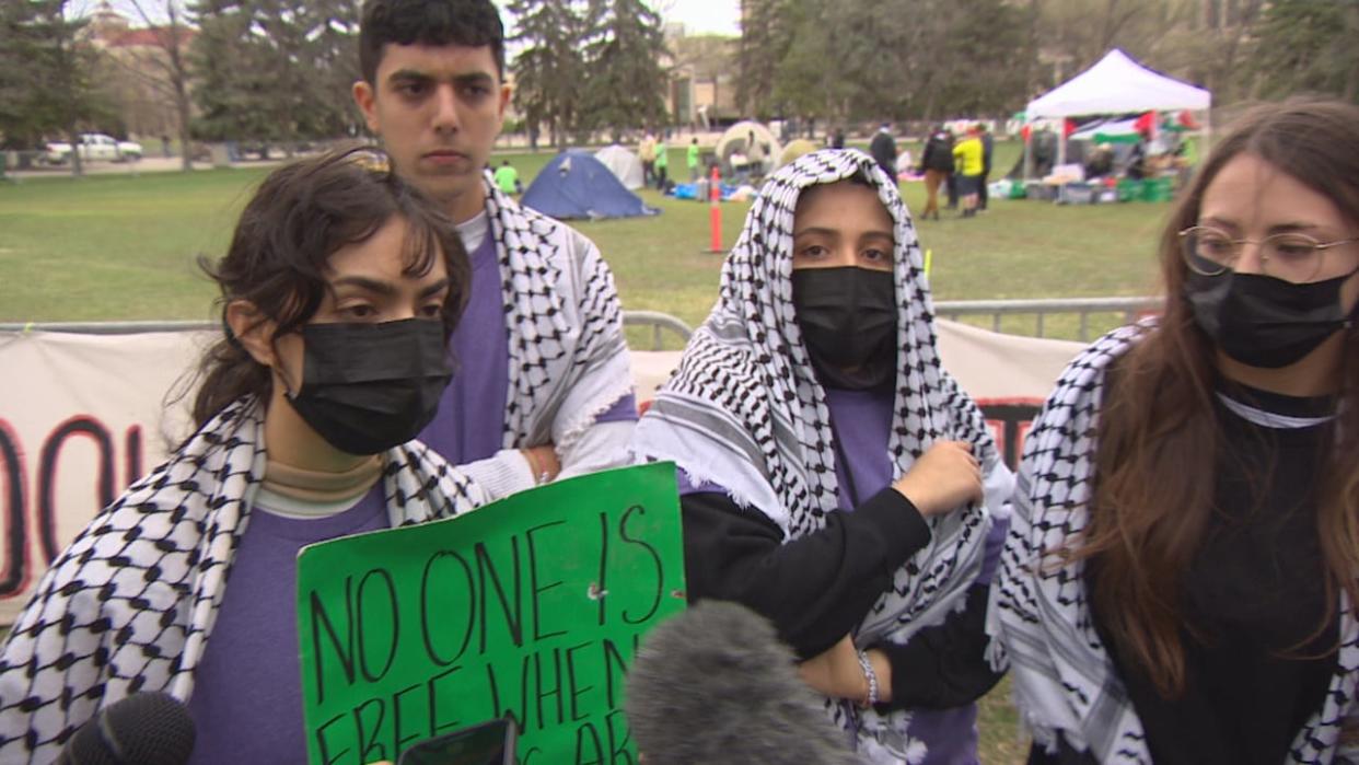 Spokespeople for the pro-Palestinian protest at the University of Manitoba speak to reporters on Tuesday. A spokesperson who identified herself as Zahra, seen here holding the green sign, said the group is demanding the university support students' right to peaceful advocacy. (Trevor Brine/CBC - image credit)