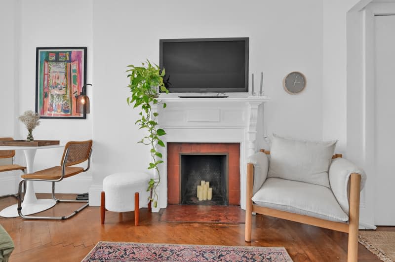 TV on a fireplace next to a lounge chair in a living room.