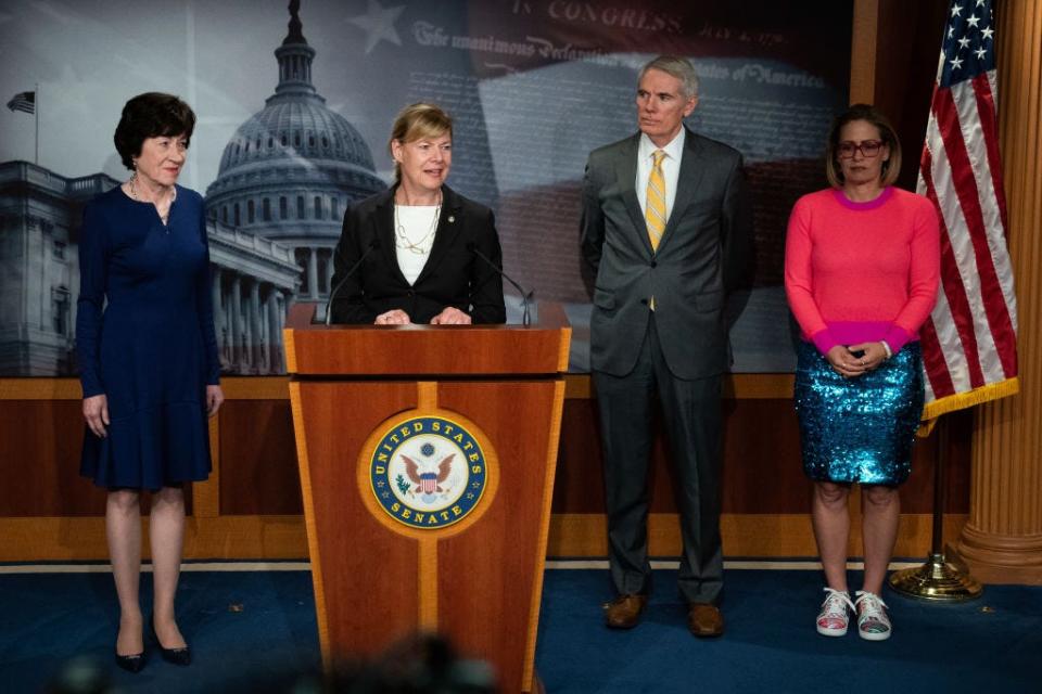 Sens. Tammy Baldwin (D-WI), Susan Collins (R-ME), Rob Portman (R-OH) and Kyrsten Sinema (D-AZ) attend a press conference. Sinema wears a hot pink sweater and teal sparkly skirt