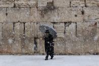 A man holding an umbrella walks as snow falls at the Western Wall in winter in Jerusalem's Old City December 12, 2013. REUTERS/Ammar Awad (JERUSALEM - Tags: RELIGION ENVIRONMENT)