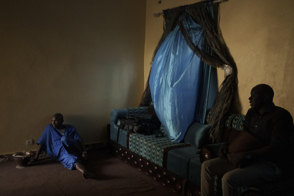 Adama Barra, right, and a relative, sit in his living room in Selibaby, Mauritania, Wednesday, Dec. 8, 2021. Barra, a local teacher, knew many of the young men who went missing after boarding a boat in Nouadhibou hoping to reach Spain's Canary Islands. (AP Photo/Felipe Dana)