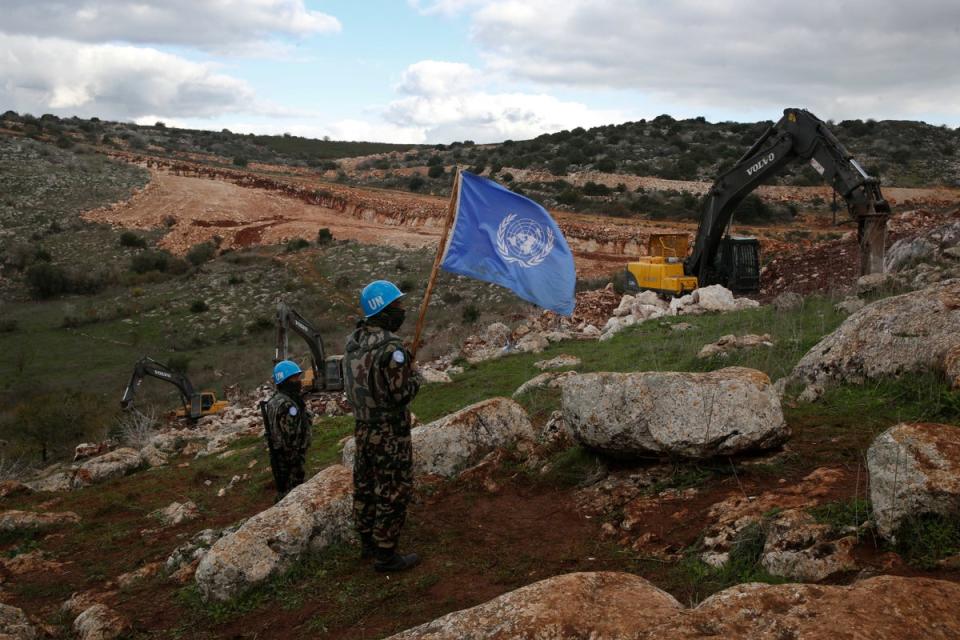 UN peacekeepers hold their flag as they observe Israeli excavators attempting to destroy tunnels built by Hezbollah near the border in 2019 (AP)