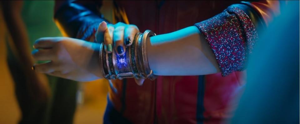 Kamala touching the thick bangle at her wrist, with the center of it glowing purple at her touch