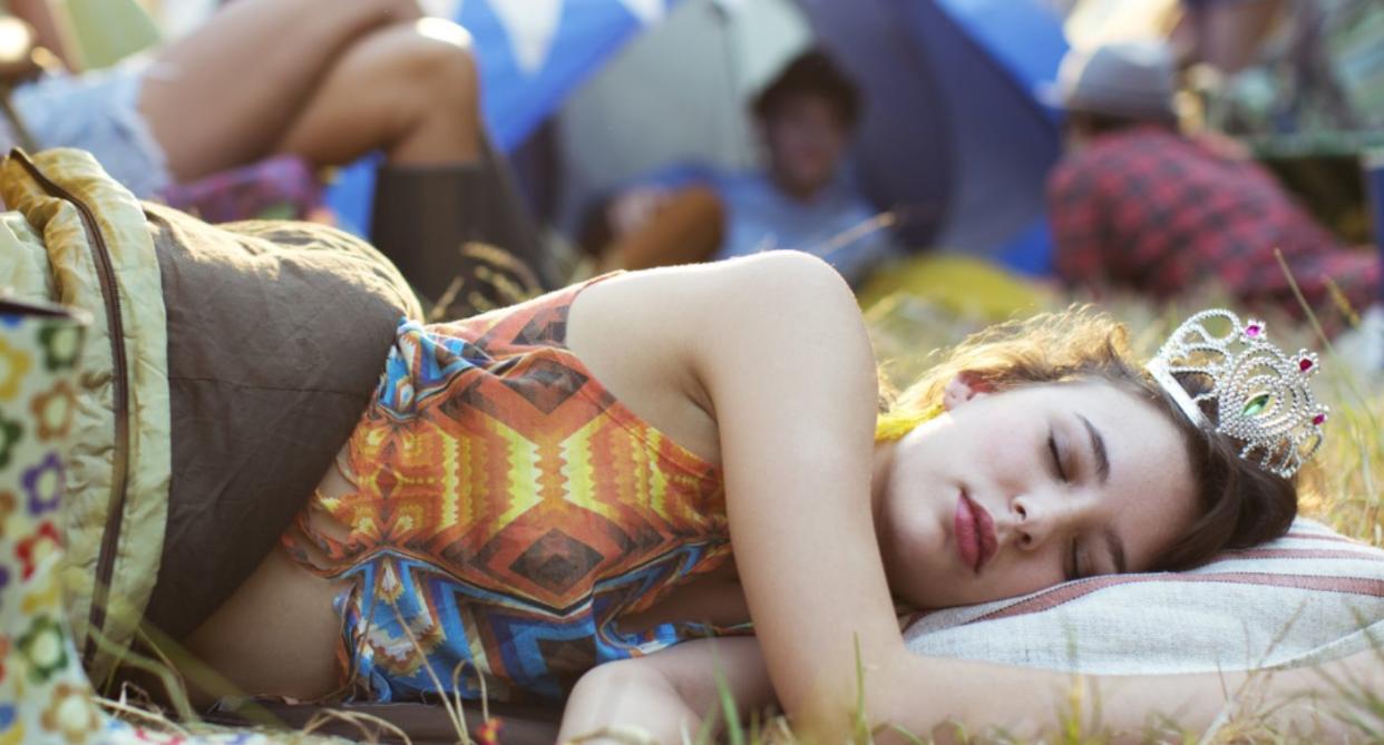 Young woman sleeping outside tent on grass at festival. (Getty Images)