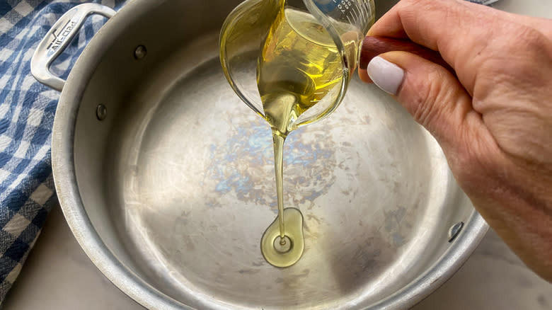 hand pouring oil into frying pan