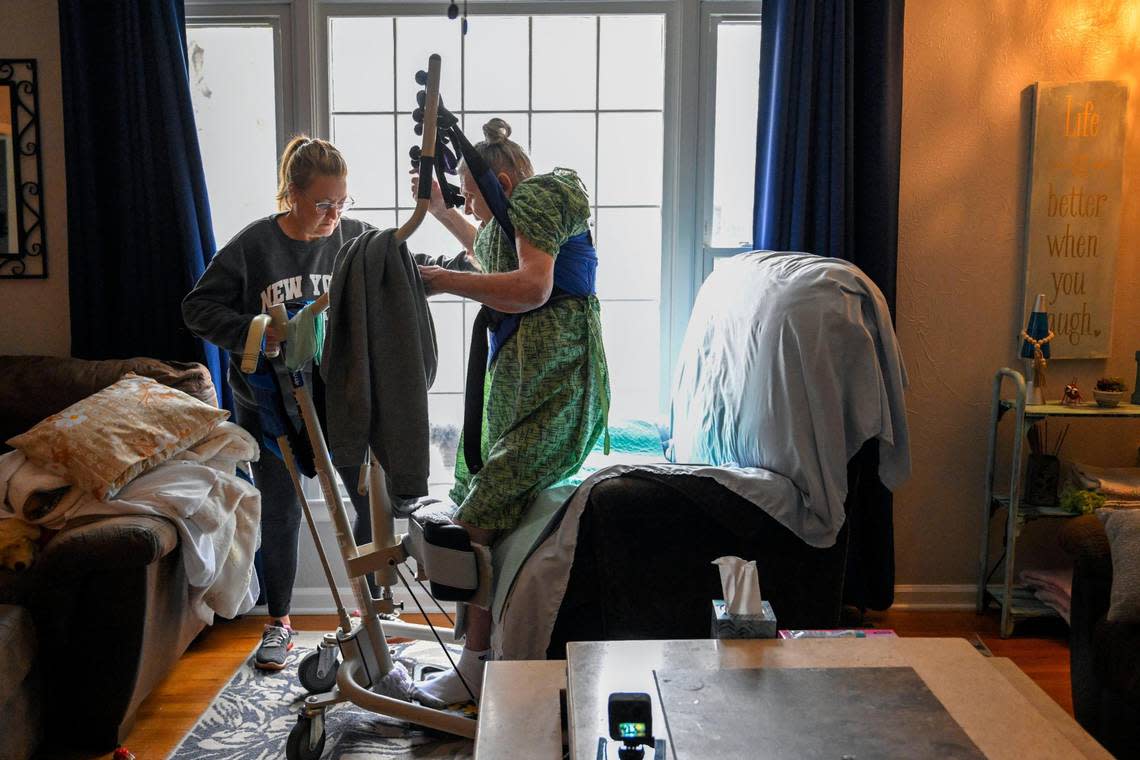 Carol Dowell uses a contraption called a sit-to-stand lift to move Ellen DeFoe from her bedroom to a recliner in the living room of Dowell’s Kansas City home. 