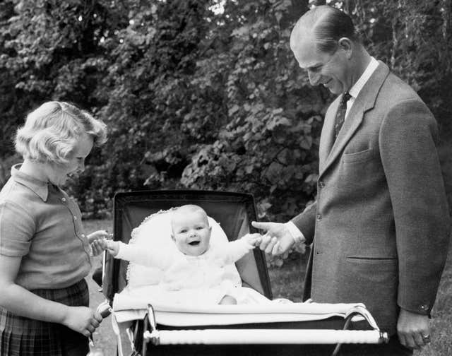 With one hand for his father, the Duke of Edinburgh, and the other for big sister Princess Anne, laughing Prince Andrew sits up in his pram in the grounds of Balmoral 