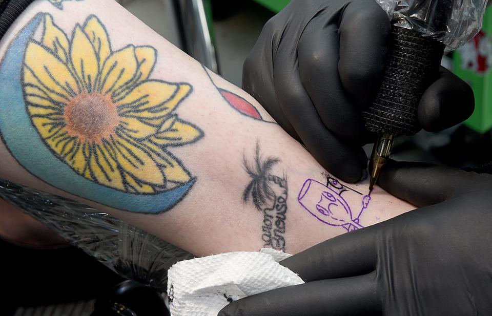 Tyler Hague, owner of The Electric Peacock, inks a tattoo of a frog holding a wine glass on the ankle of Megan Bedford on Thursday during a half-price tattoo special the shop is running Thursday through Saturday.