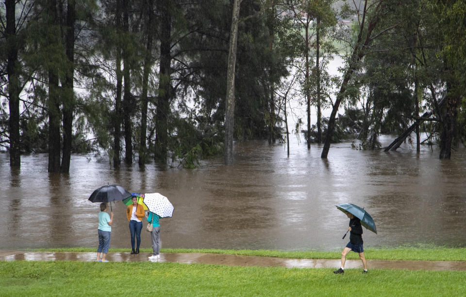 People stand on the banks of the Nepean River at Jamisontown on the western outskirts of Sydney Monday, March 22, 2021. Australia's most populous state of New South Wales has issued more evacuation orders following the worst flooding in decades. (AP Photo/Mark Baker)