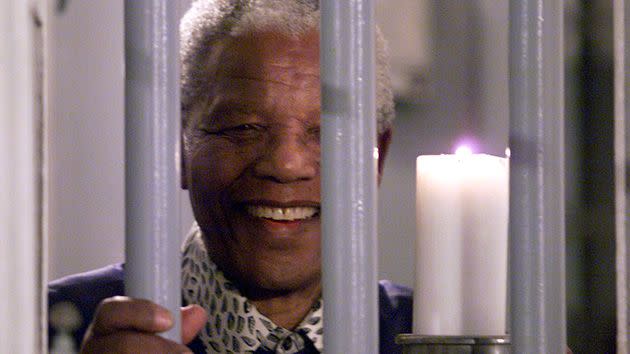 Mandela holds a symbolic millennium candle through the bars of the prison cell in which he was incarcerated on Robben Island. Photo: Getty.