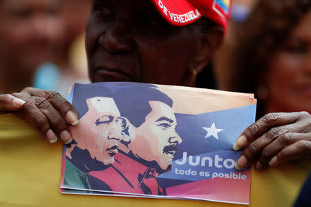 A supporter of Venezuela's President Nicolas Maduro holds a banner depicting Maduro and late President Hugo Chavez, during a campaign rally in Caracas, Venezuela May 16, 2018. The banner reads: "Together, everything is possible". Picture taken May 16, 2018. REUTERS/Carlos Garcia Rawlins