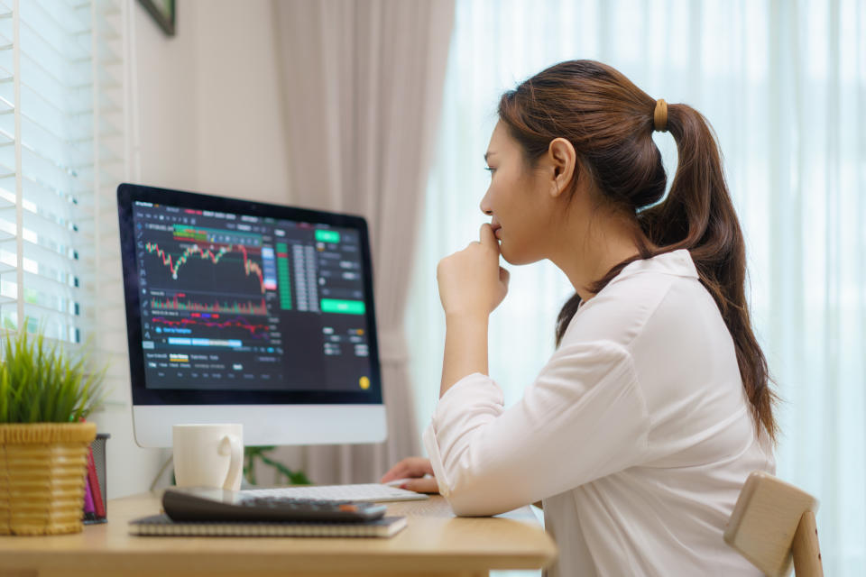 Woman sitting at a desk at in front of computer showing trading charts.