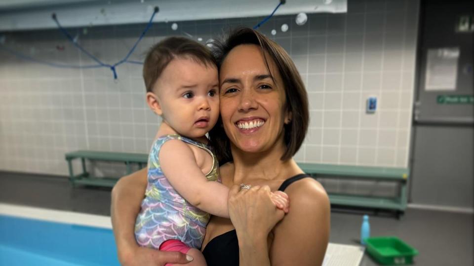 mother in bikini holding daughter by swimming pool