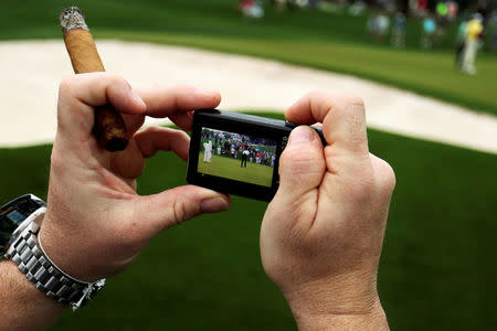 A patron holds a lit cigar and a camera during the third day of practice rounds before The Masters at Augusta National Golf Club in Augusta, Georgia, U.S. April 5, 2017. REUTERS/Jonathan Ernst